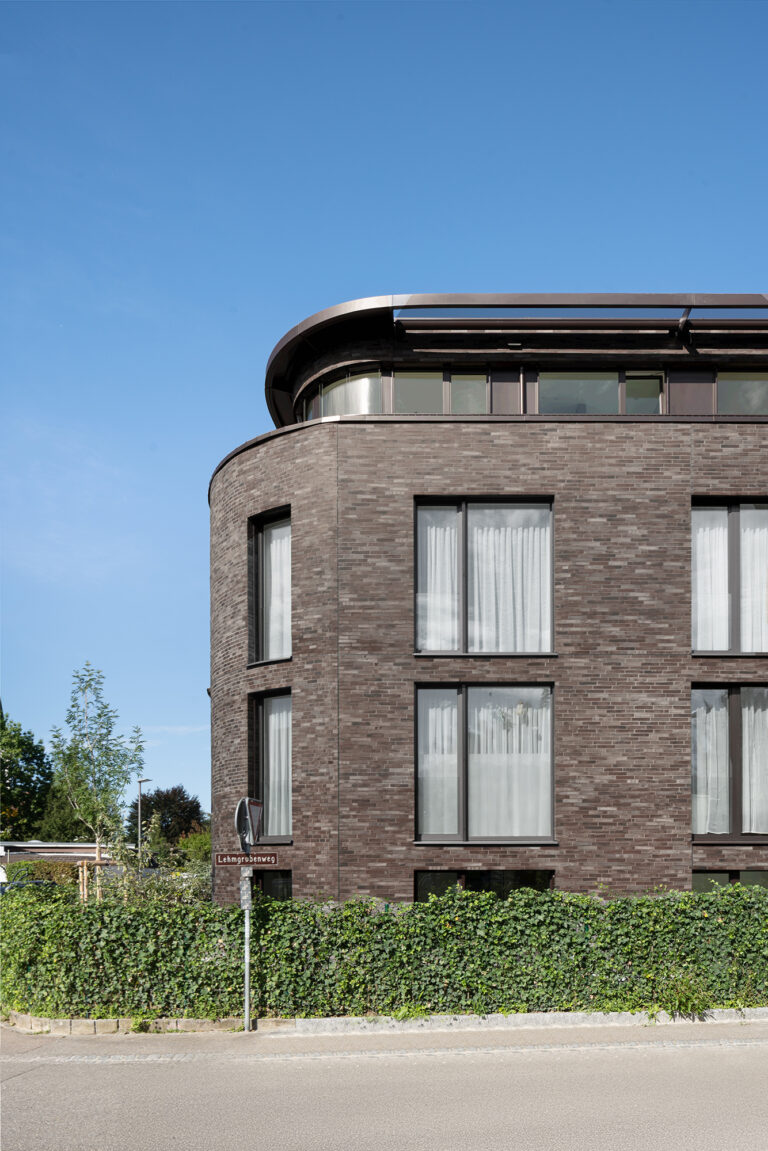 Foto eines Ausschnittes von einem Mehrfamilienhaus mit dunkel-braunem Klinker vor einem blauen Himmel.
