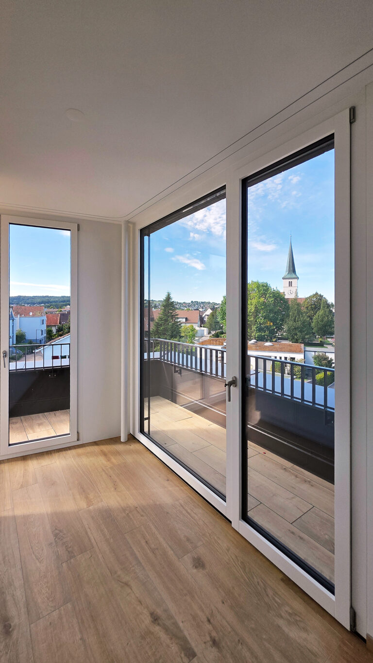 Foto-Ausschnitt eines Raumes mit Sicht auf die Terrasse und ausgezogener Markise und Blick ins Grüne.