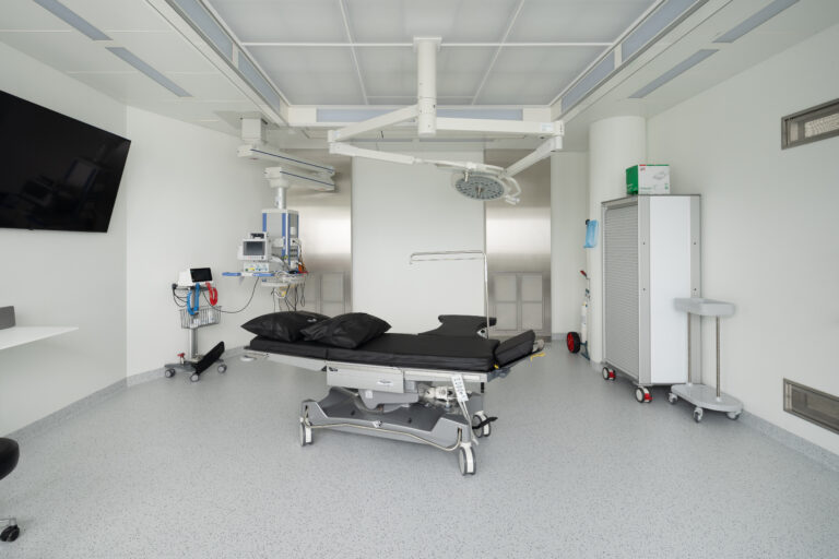 Foto eines modernen hellen Behandlungsraumes mit weissen Wänden, hellem Boden und schwarzer Liege.