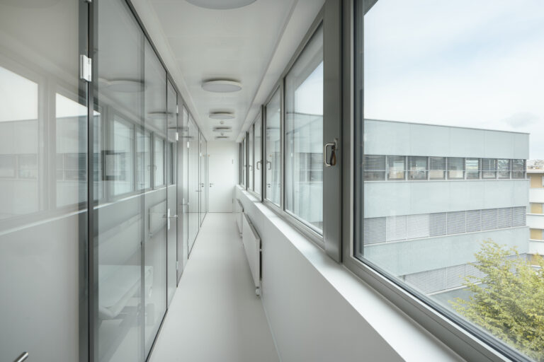 Foto eines Ganges zwischen langer Fensterfront und langer Glasfront.