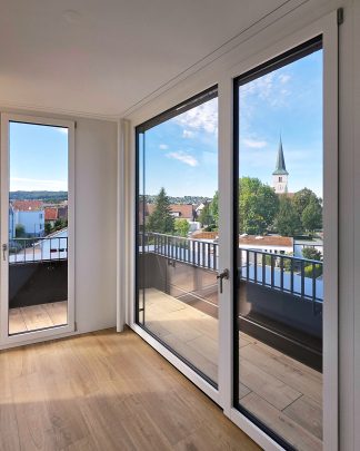 Foto-Ausschnitt eines Raumes mit Sicht auf die Terrasse und ausgezogener Markise und Blick ins Grüne.