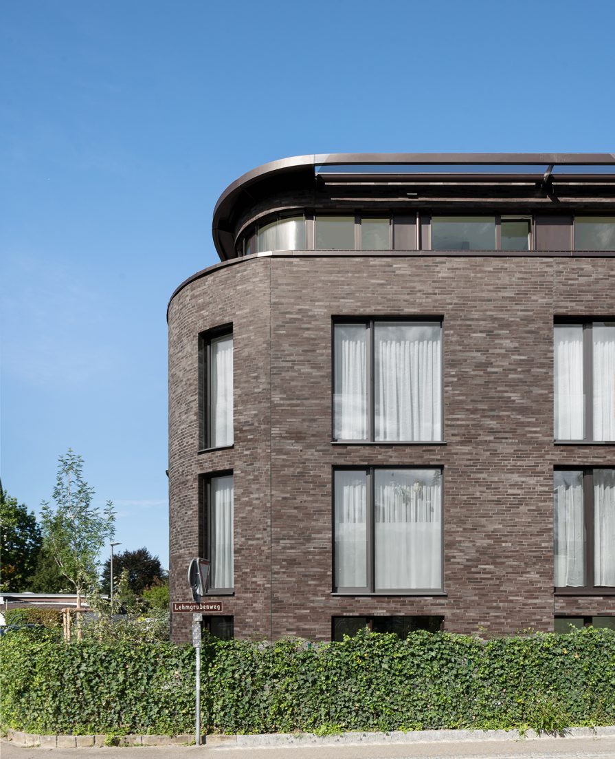 Foto eines Ausschnittes von einem Mehrfamilienhaus mit dunkel-braunem Klinker vor einem blauen Himmel.