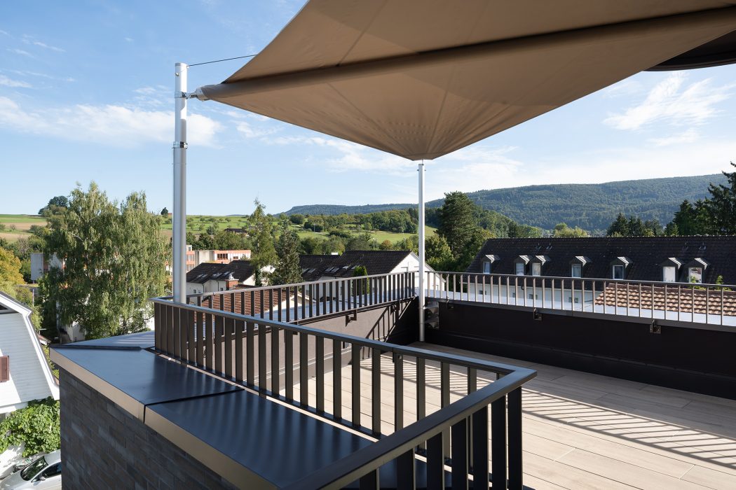 Bild mit Balkon und offener Markise in warmen Farben von dem aus man die Aussicht auf die grüne Umgebung sieht.