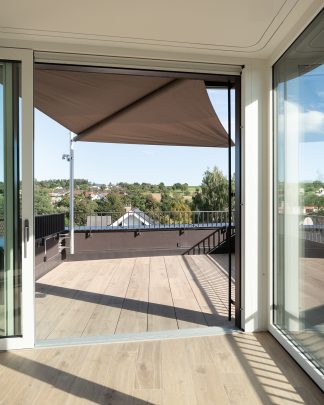 Foto-Ausschnitt eines Lichtdurchfluteten warmen Raumes mit Sicht auf die Terrasse und ausgezogener Markise und Blick ins Grüne.