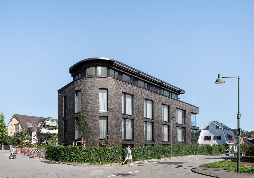 Foto einer Seitenansicht einer Rundung eines Mehrfamilienhauses mit dunklem warmem Klinker vor blauem Himmel.
