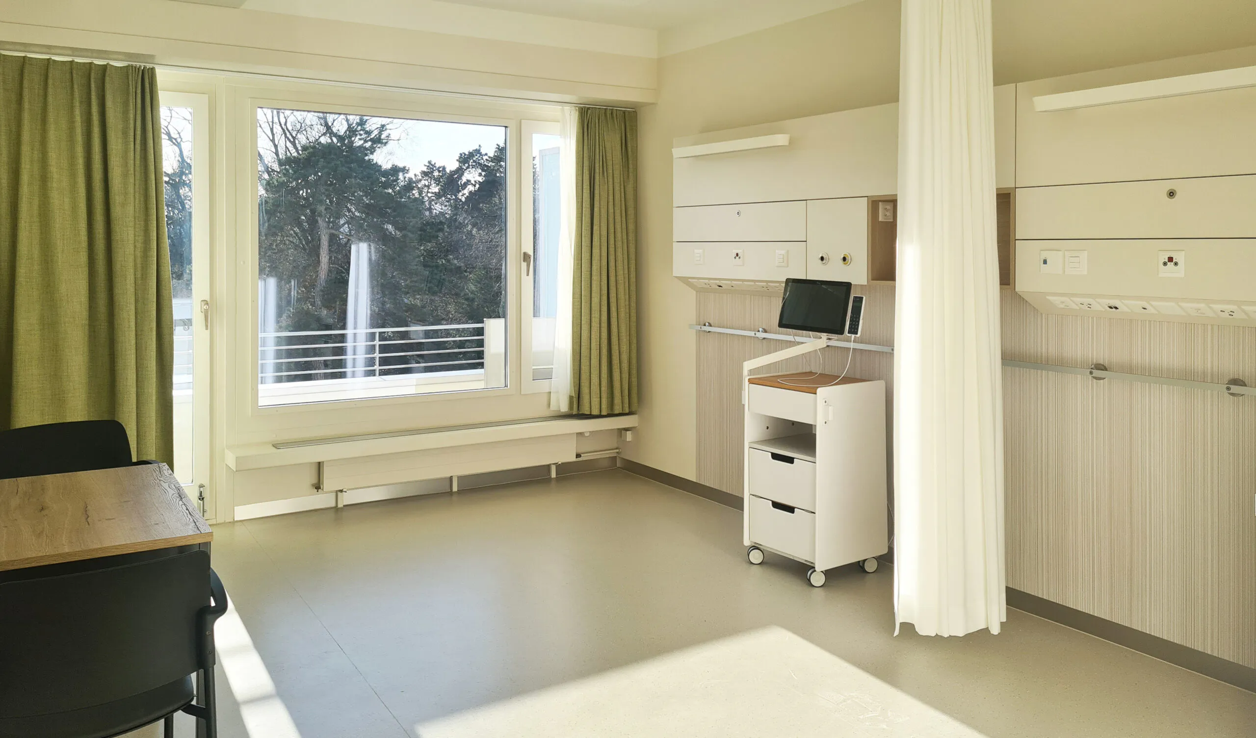Spitalzimmer vom St. Claraspital mit hellen einheitlichen und warmen Farben mit Blick auf den Spitalgarten.